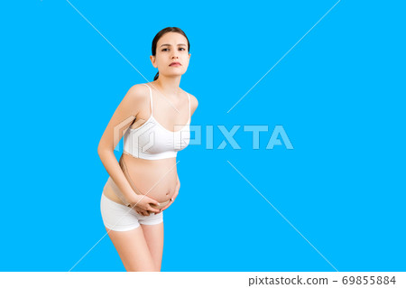 Portrait of supporting bandage against backache on pregnant woman in underwear at blue background with copy space. Mother is suffering from pain in the back. Orthopedic abdominal support belt concept Portrait of supporting bandage against backache on pregnant woman in underwear at blue background with copy space. Mother is suffering from pain in the back. Orthopedic abdominal support belt concept 69855884
