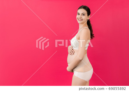Portrait of pregnant woman in underwear wearing maternity belt to reduce pain in the back at pink background with copy space. Orthopedic abdominal support belt concept Portrait of pregnant woman in underwear wearing maternity belt to reduce pain in the back at pink background with copy space. Orthopedic abdominal support belt concept 69855892