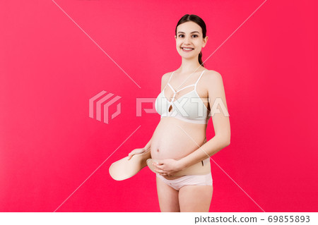 Portrait of pregnant woman in colorful underwear putting on a bandage at pink background with copy space. Orthopedic abdominal support belt concept Portrait of pregnant woman in colorful underwear putting on a bandage at pink background with copy space. Orthopedic abdominal support belt concept 69855893