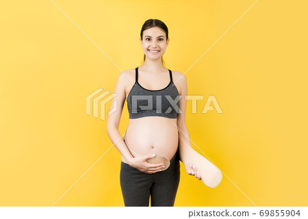Portrait of pregnant woman putting on a bandage at yellow background with copy space. Orthopedic abdominal support belt concept Portrait of pregnant woman putting on a bandage at yellow background with copy space. Orthopedic abdominal support belt concept 69855904