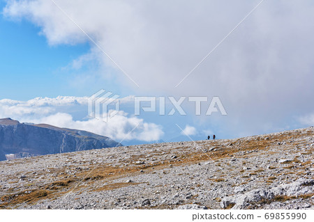 alpine plateau covered with white stones, and a couple of hikers in the distance alpine plateau covered with white stones, and a couple of hikers in the distance 69855990