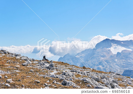 alpine plateau, covered with dry grass and white stones, with a traveler sitting against mountains 69856018