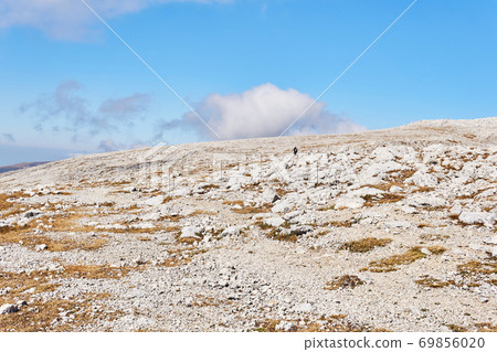 alpine plateau covered with white stones, and a couple of travelers in the distance alpine plateau covered with white stones, and a couple of travelers in the distance 69856020