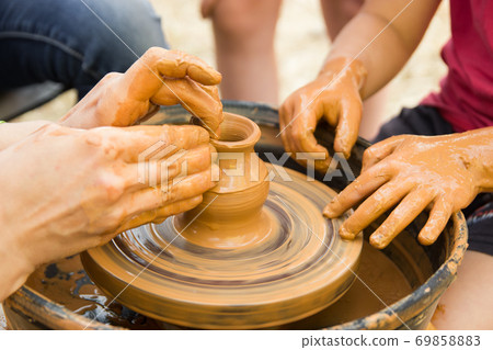 A close up view on ceramic production process on potter's wheel with children. Clay crafts with kids concept A close up view on ceramic production process on potter's wheel with children. Clay crafts with kids concept 69858883
