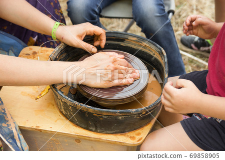 A close up view on ceramic production process on potter's wheel with children. Clay crafts with kids concept 69858905