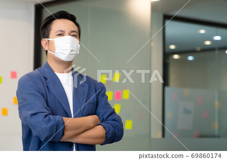 Business asian man stand and wear masks and cross arm in the office. Business asian man stand and wear masks and cross arm in the office. 69860174