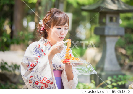 在夏日祭上吃日式炒麵的穿著浴衣的女人 照片素材 圖片 圖庫