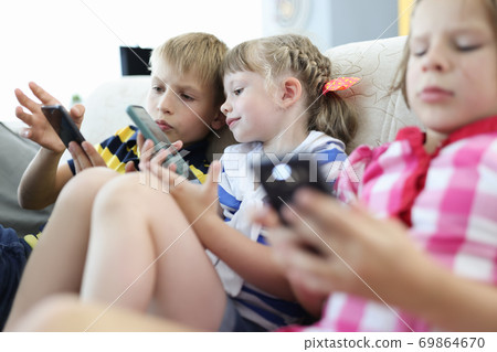 Children sit on couch and play smartphones. 69864670