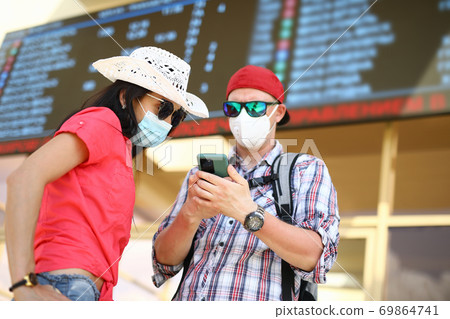 Man and woman in medical protective masks at train station next to information board. 69864741