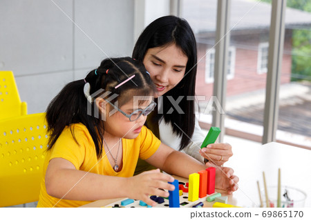 Asian girl with Down's syndrome play puzzle toy with her teacher in classroom. 69865170