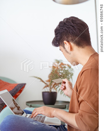 Young man shopping online with credit card and laptop at home 69866748