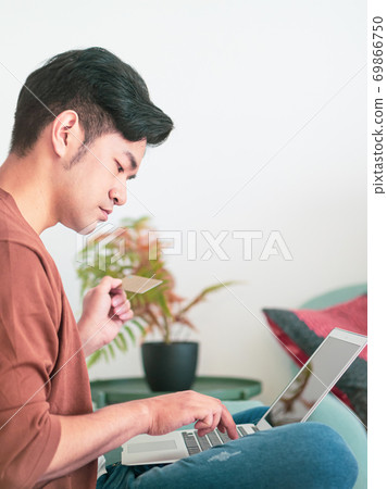 Young man shopping online with credit card and laptop at home 69866750