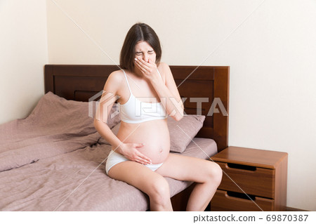 Pregnant suffering with nausea. Pregnancy symptoms, expectation toxicosis. Young vomiting woman sitting on bed. parenthood concept 69870387
