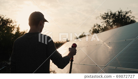 Silhouette of a man washing a solar power plant panel Silhouette of a man washing a solar power plant panel 69872727