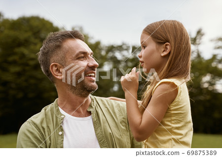 Daughter and daddy. Cute little girl spending time with father while visiting park on a summer day, they are talking and smiling Daughter and daddy. Cute little girl spending time with father while visiting park on a summer day, they are talking and smiling 69875389
