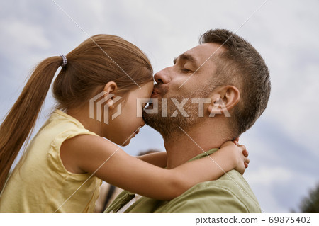 My little girl. Young loving father kissing his cute daughter in forehead while spending time together outdoors, blue sky on the background 69875402