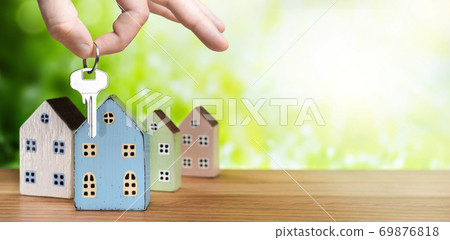 Hand with house key and miniature houses on green nature background Hand with house key and miniature houses on green nature background 69876818