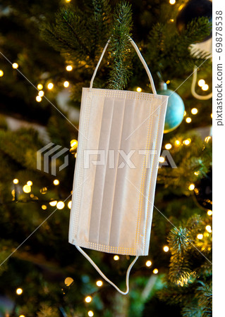 Christmas tree with Coronavirus face mask hanging in tree, decorated with Covid-19 safety mask and Christmas balls for bright Christmas Christmas tree with Coronavirus face mask hanging in tree, decorated with Covid-19 safety mask and Christmas balls for bright Christmas 69878538