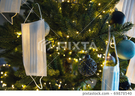 Christmas tree with Coronavirus face mask hanging in tree, decorated with Covid-19 safety mask and Christmas balls for bright Christmas Christmas tree with Coronavirus face mask hanging in tree, decorated with Covid-19 safety mask and Christmas balls for bright Christmas 69878540