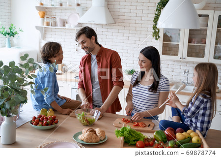 Preparing a salad. Lovely family of four cooking together in the modern kitchen at home Preparing a salad. Lovely family of four cooking together in the modern kitchen at home 69878774