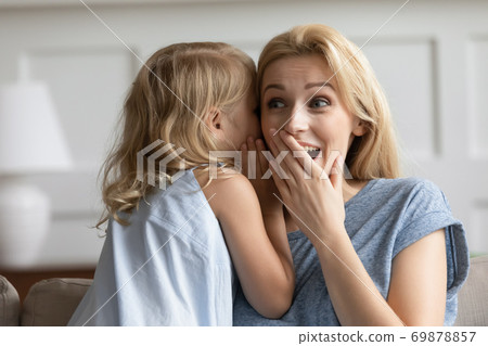 Naughty preschool girl whispering joke on amazed grown sister ear Naughty preschool girl whispering joke on amazed grown sister ear 69878857