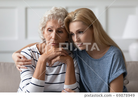 Sad grownup daughter sitting on sofa hugging desperate elderly mother Sad grownup daughter sitting on sofa hugging desperate elderly mother 69878949