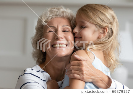 Affectionate elderly grandma holding on tight to little girl grandkid Affectionate elderly grandma holding on tight to little girl grandkid 69879137