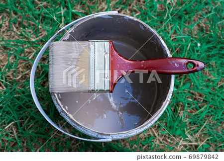 Paint brush placed on the paint bucket in the green grass area Paint brush placed on the paint bucket in the green grass area 69879842