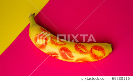 Red lipstick on a yellow banana on a pink background. Red lipstick on a yellow banana on a pink background. 69880116