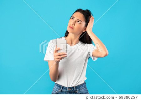 Confused upset young woman holding mobile phone Confused upset young woman holding mobile phone 69880257