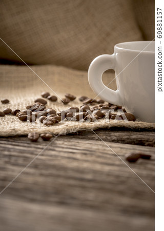 Low angle view of coffee beans scattered on linen cloth lying on textured wooden desk Low angle view of coffee beans scattered on linen cloth lying on textured wooden desk 69881157