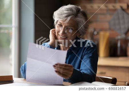 Mature 60s woman read paper postal correspondence at home 69881657