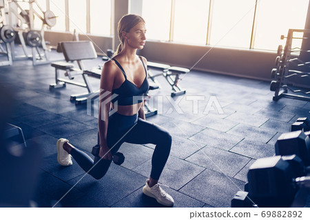 Beautiful girl doing lunges exercise with dumbbells in gym Beautiful girl doing lunges exercise with dumbbells in gym 69882892