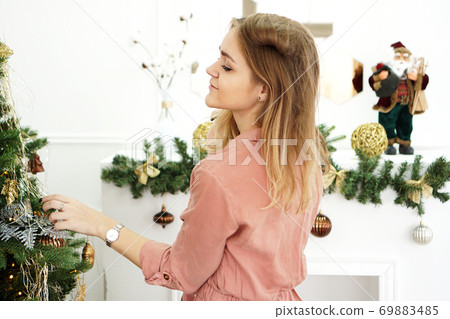 Beautiful young woman decorating a Christmas tree Beautiful young woman decorating a Christmas tree 69883485