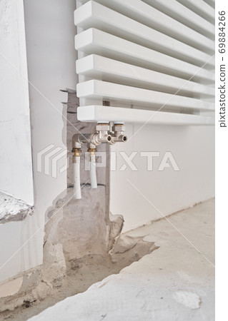 connection heating pipes to white Radiator in a new apartment under construction. Work As A Plumber, mounting water heating radiator on the white wall indoors connection heating pipes to white Radiator in a new apartment under construction. Work As A Plumber, mounting water heating radiator on the white wall indoors 69884266