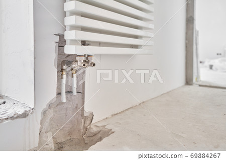connection heating pipes to white Radiator in a new apartment under construction. Work As A Plumber, mounting water heating radiator on the white wall indoors connection heating pipes to white Radiator in a new apartment under construction. Work As A Plumber, mounting water heating radiator on the white wall indoors 69884267