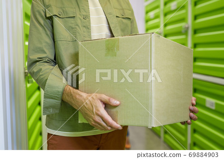 Unrecognizable Man Holding Box in Self Storage Unit 69884903