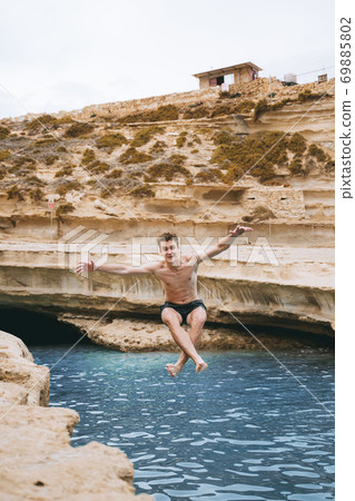 A man swimming in a body of water. Jumping from rock to the water with salto A man swimming in a body of water. Jumping from rock to the water with salto 69885802