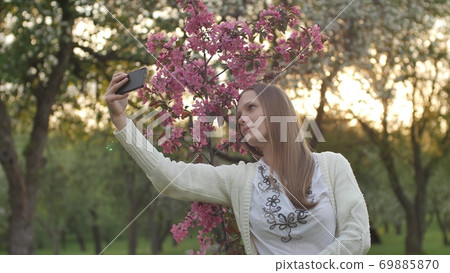 Girl makes selfie in the garden. An attractive red-haired woman smiles making selfi using a mobile Girl makes selfie in the garden. An attractive red-haired woman smiles making selfi using a mobile 69885870