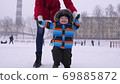 Mother leads the hands of a small smiling baby in the snow in the park. The first steps of the child 69885872