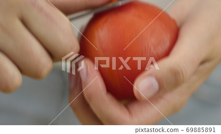 Man or woman peels off a tomato with a knife. Preparation of products for cooking Man or woman peels off a tomato with a knife. Preparation of products for cooking 69885891