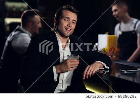 portrait of a young man in a shirt and jacket at the bar with a cocktail in his hands portrait of a young man in a shirt and jacket at the bar with a cocktail in his hands 69886282