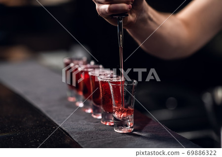 the bartender fills shots with red liquor from a bottle on the bar the bartender fills shots with red liquor from a bottle on the bar 69886322