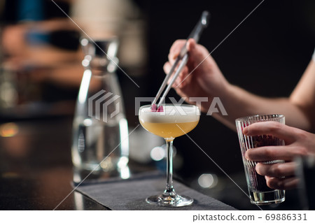Close-up of a glass with a beautiful delicious cocktail standing on the table in a restaurant. The bartender creates an alcoholic drink for women Close-up of a glass with a beautiful delicious cocktail standing on the table in a restaurant. The bartender creates an alcoholic drink for women 69886331