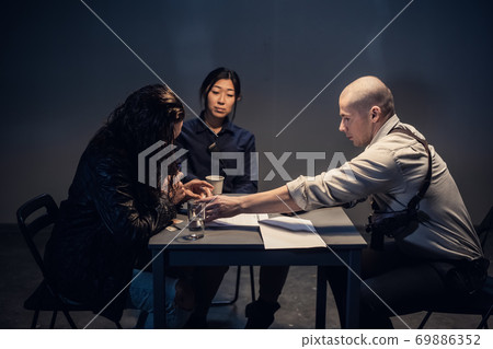 A police investigator with a gun in a holster meets with a man suspected of theft in the presence of a lawyer at the police station. A police investigator with a gun in a holster meets with a man suspected of theft in the presence of a lawyer at the police station. 69886352