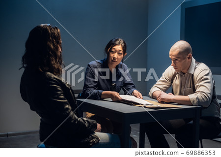 The murder suspect is in the interrogation room with a grim investigator and lawyer. The murder suspect is in the interrogation room with a grim investigator and lawyer. 69886353