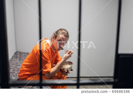 Dinner in a prison cell. A prisoner eats tasteless food from an iron bowl under guard behind bars. 69886386