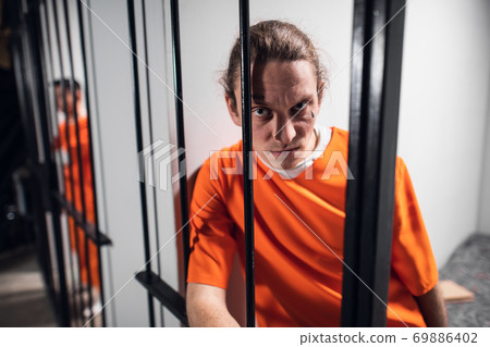 A desperate criminal maniac with tattoos in a solitary cell is kept behind bars. A hard look at the camera. 69886402