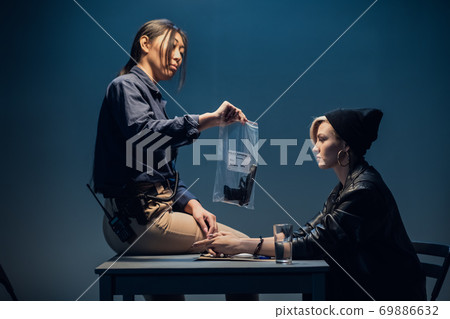 An experienced investigator during an interrogation at a police station shows the criminal girl the found crime weapon An experienced investigator during an interrogation at a police station shows the criminal girl the found crime weapon 69886632
