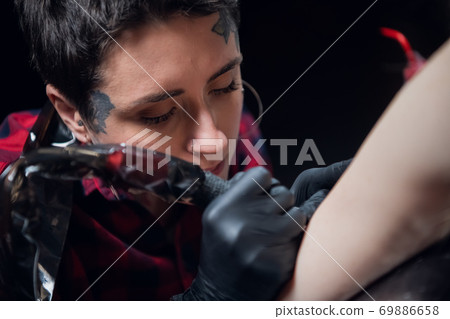 Attractive girl tattoo artist at work, makes a tattoo on the arm of a young woman 69886658